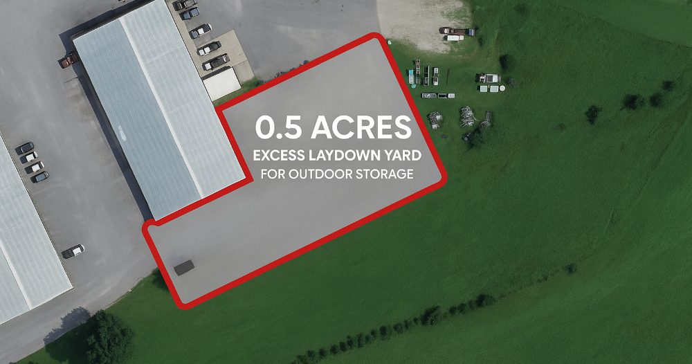 Aerial of 101 Austin Bradley Lane with a red outline marking a 0.5-acre excess laydown yard for outdoor storage beside the building, and open grass acreage to the east