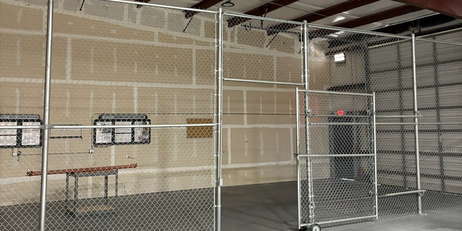 Chain-link secured storage cage inside the warehouse at 101 Austin Bradley Lane, with a rolling gate and a workbench along the block wall