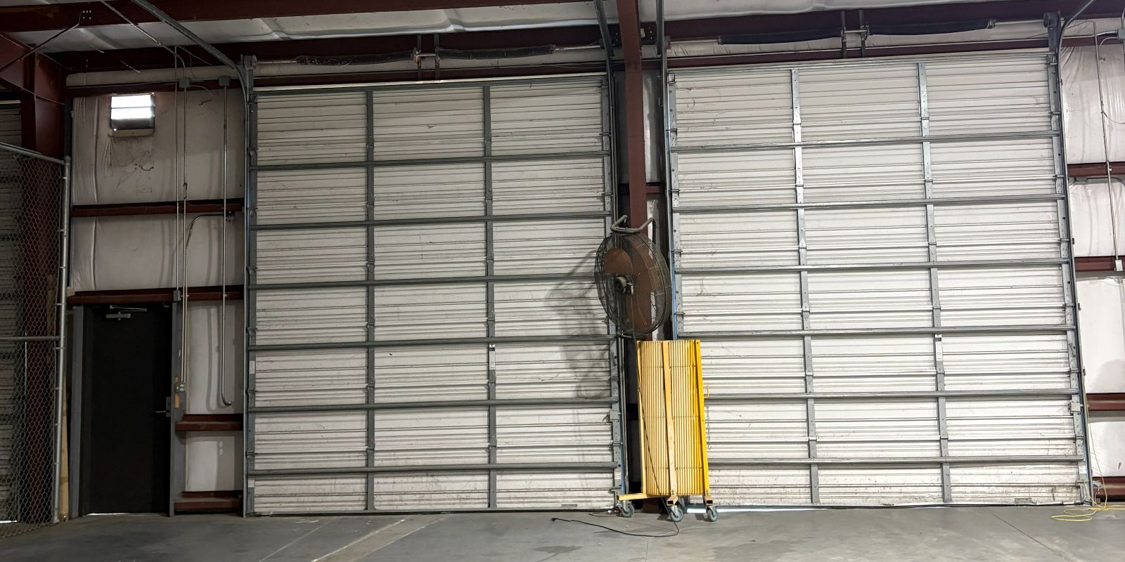 Interior of the clear-span warehouse at 101 Austin Bradley Lane, with two full-height drive-in overhead doors, exposed steel framing, and a sealed concrete floor