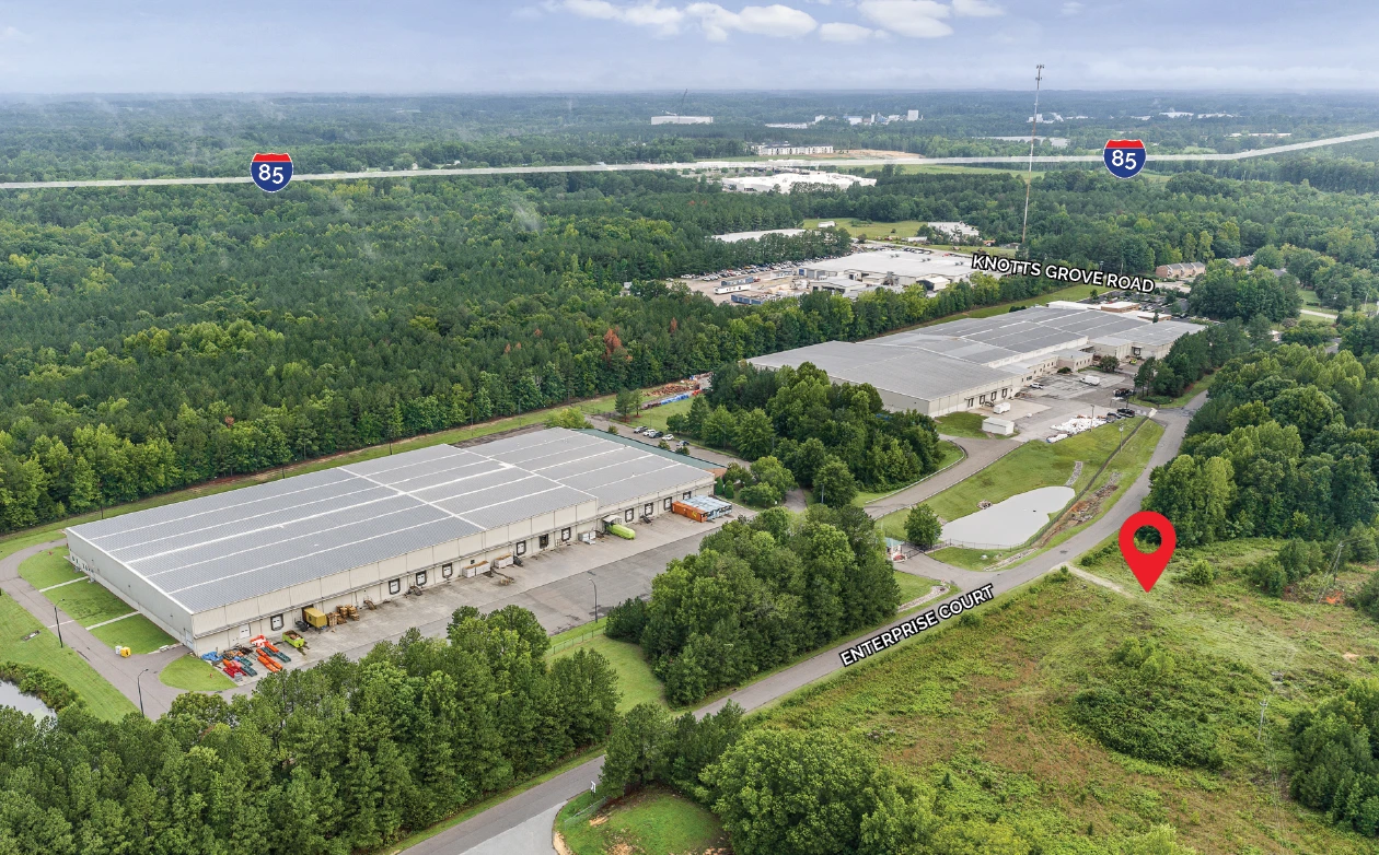 Aerial of the 105 Enterprise Court site, an open lot marked with a red pin on Enterprise Court, beside large industrial buildings off Knotts Grove Road with I-85 crossing the background