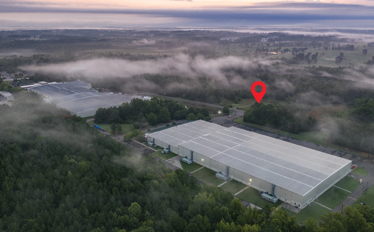 Aerial at dawn over a large industrial building toward the 105 Enterprise Court site, marked with a red pin, with low fog over the surrounding woods and fields