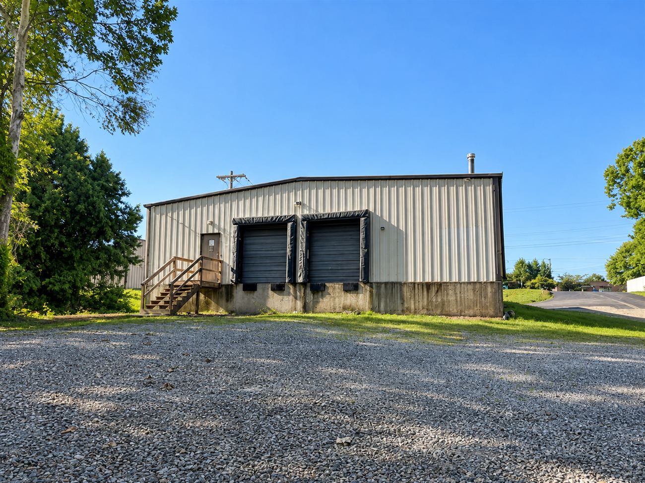 Rear elevation of 1310 Starr Drive showing two dock-height overhead doors with dock seals set into a raised concrete base, a side entry with wooden steps, and a gravel dock court