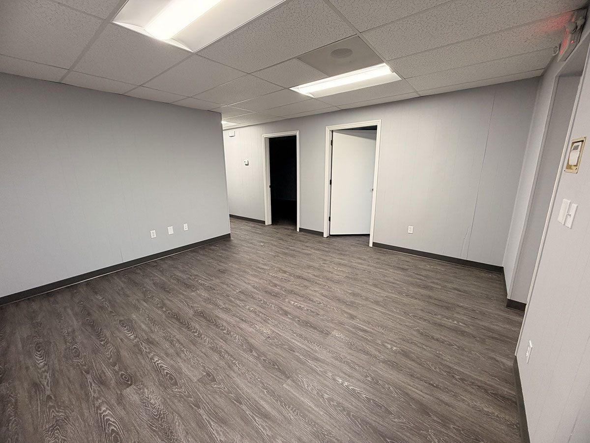 Reception area at 1310 Starr Drive with grey vinyl plank flooring, light grey walls, a drop ceiling with recessed lighting, and two doorways leading through to the private offices