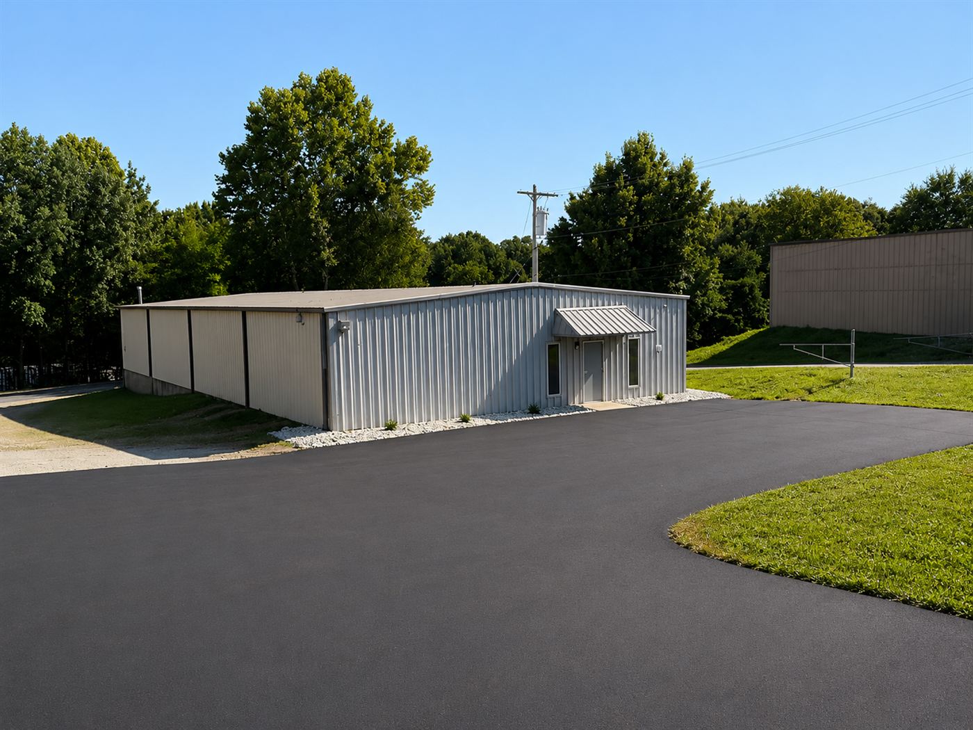 The newly paved asphalt lot wrapping the front and side of 1310 Starr Drive, with the building's entry canopy at the far end and a gravel drive continuing past the corner