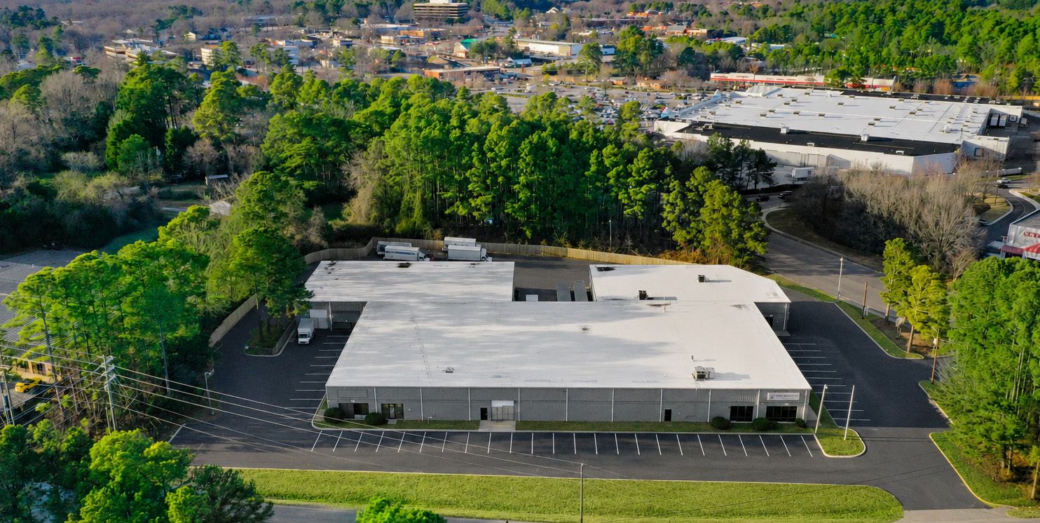 Aerial view of 1904 New Hope Church Road, a multi-tenant industrial building in Raleigh, North Carolina, with a white roof, striped parking on two sides, and Walmart-anchored retail beyond the tree line
