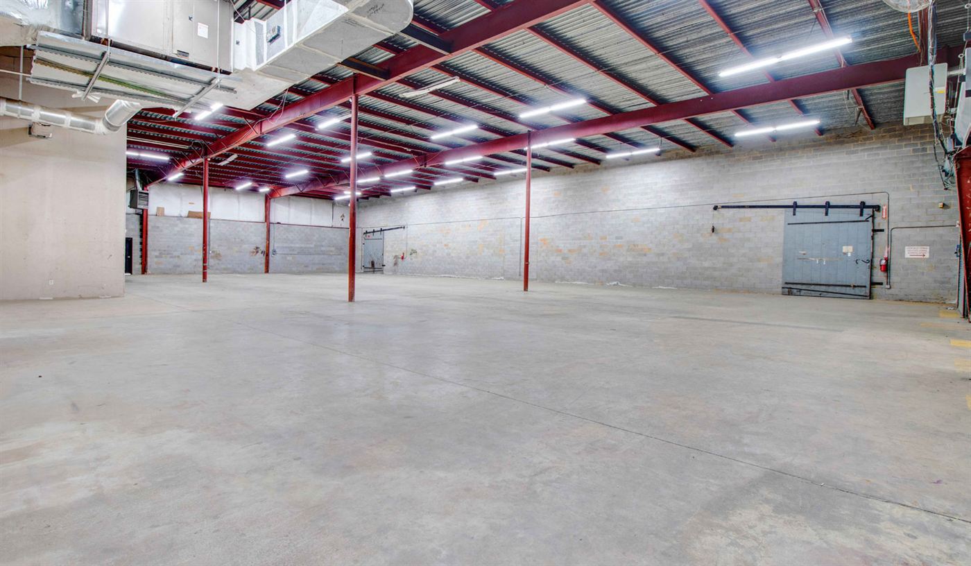 Second warehouse view at 1904 New Hope Church Road showing block walls, red steel columns, sliding steel fire doors, exposed ductwork, and an open concrete floor