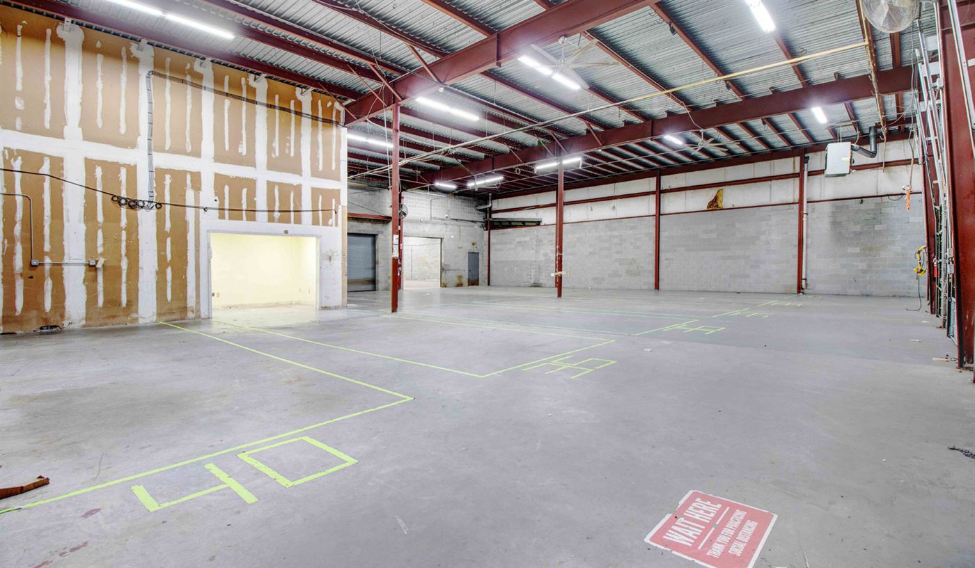 Warehouse bay at 1904 New Hope Church Road with taller clear height, ceiling fans, block and drywall partition walls, and yellow staging lines marked on the concrete floor