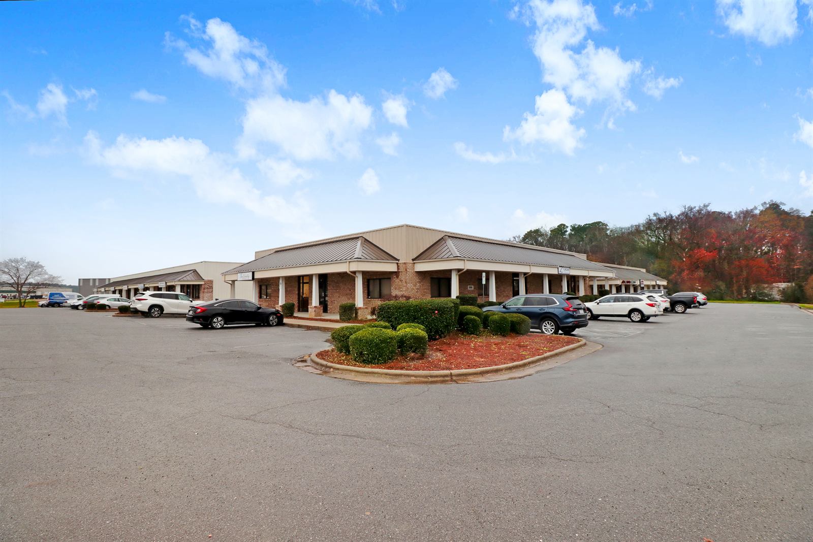 Ground-level view of the front building at 1990 Allen Road, a brick and metal-clad single-storey building with a covered colonnade walkway, hipped standing-seam roof, storefront entries, and cars parked along the frontage