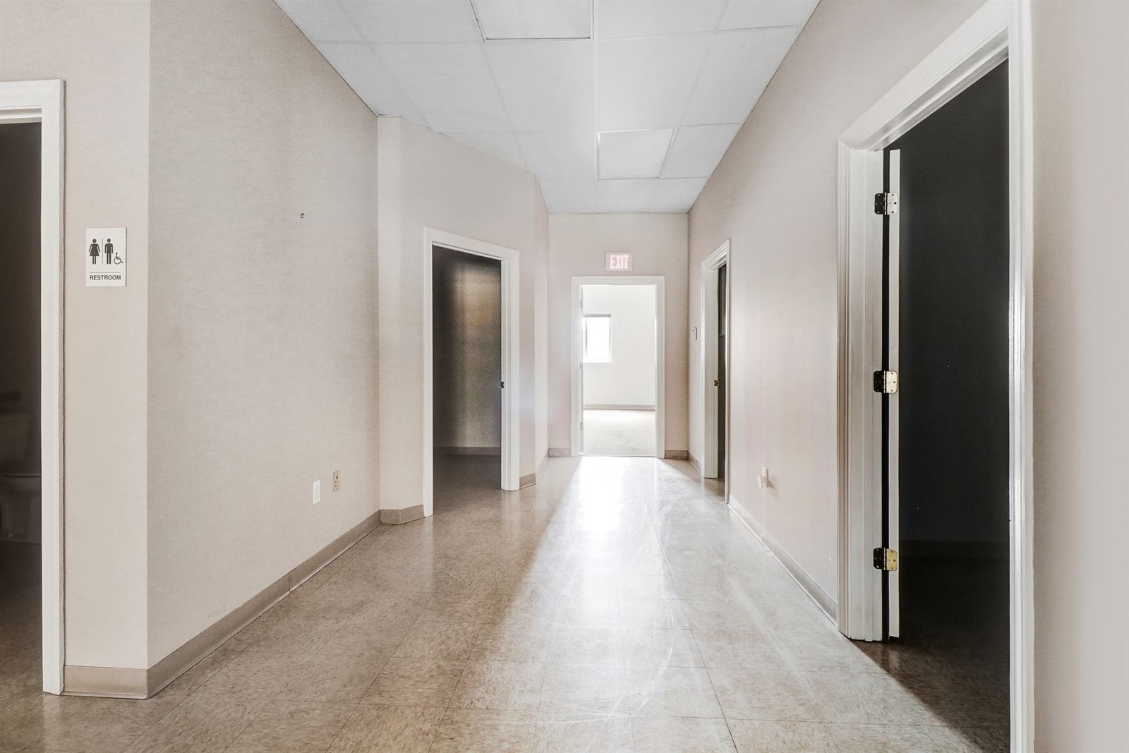 Interior corridor of the available suite at 1990 Allen Road running past several private office doorways to a lit rear room, with an ADA restroom sign at the near wall and tile flooring throughout