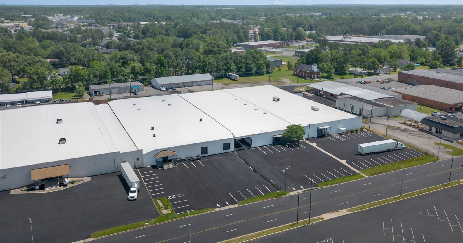 Aerial view along the Lee Avenue Industrial Complex, showing the length of the warehouse roof, the loading elevation, and the striped surface parking beside Lee Avenue