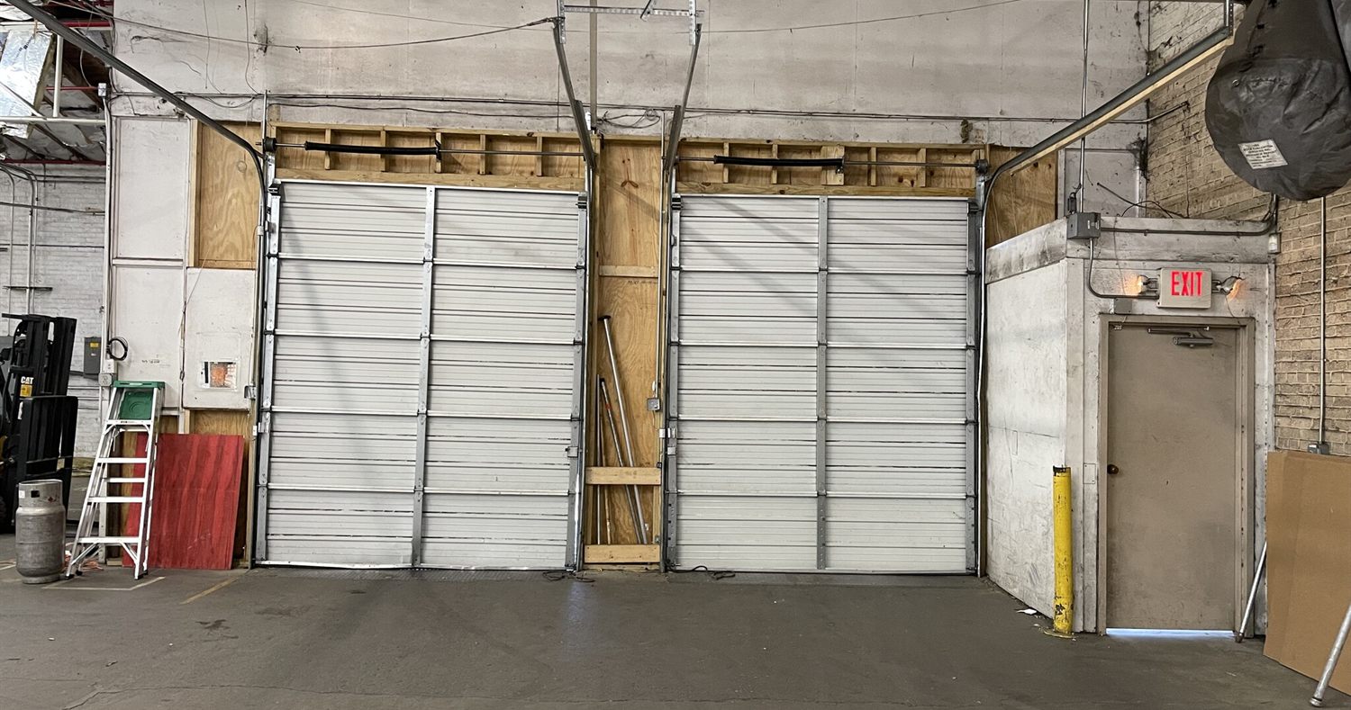 Two interior drive-in overhead doors at 2613 Lee Avenue set into a painted wall, with a forklift parked to the side and an exit door alongside