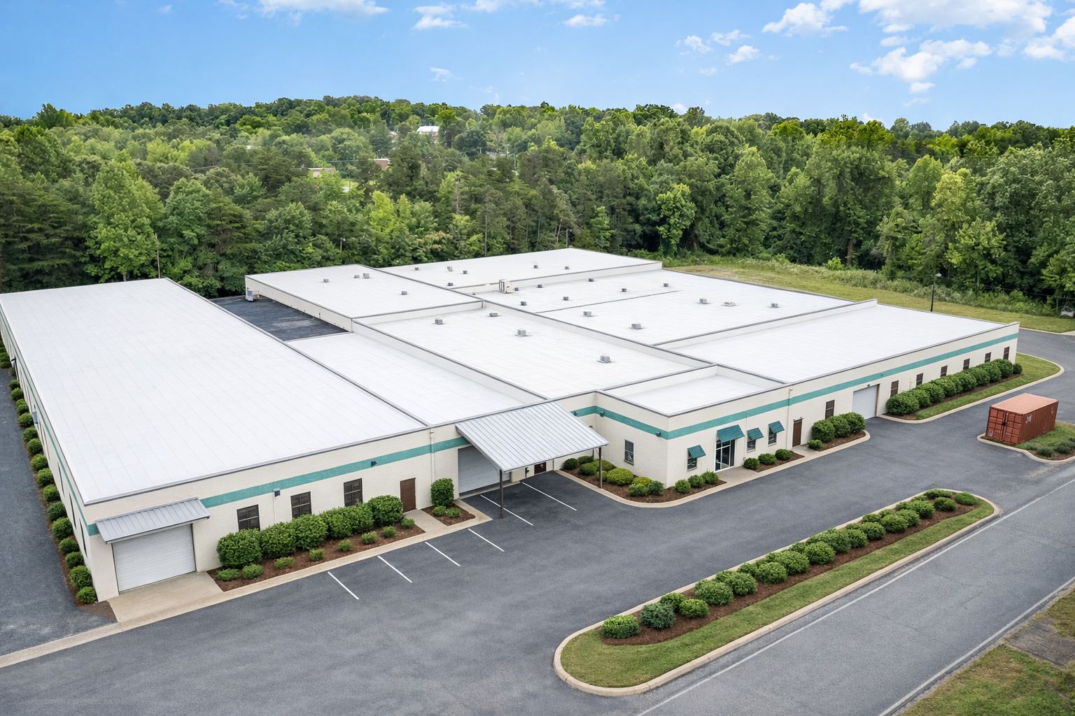 Aerial view of 314 Mandustry Street, a single-story multi-tenant industrial building in High Point, North Carolina, with white roofs, a teal accent band, drive-in doors along the front elevation, and a paved parking field