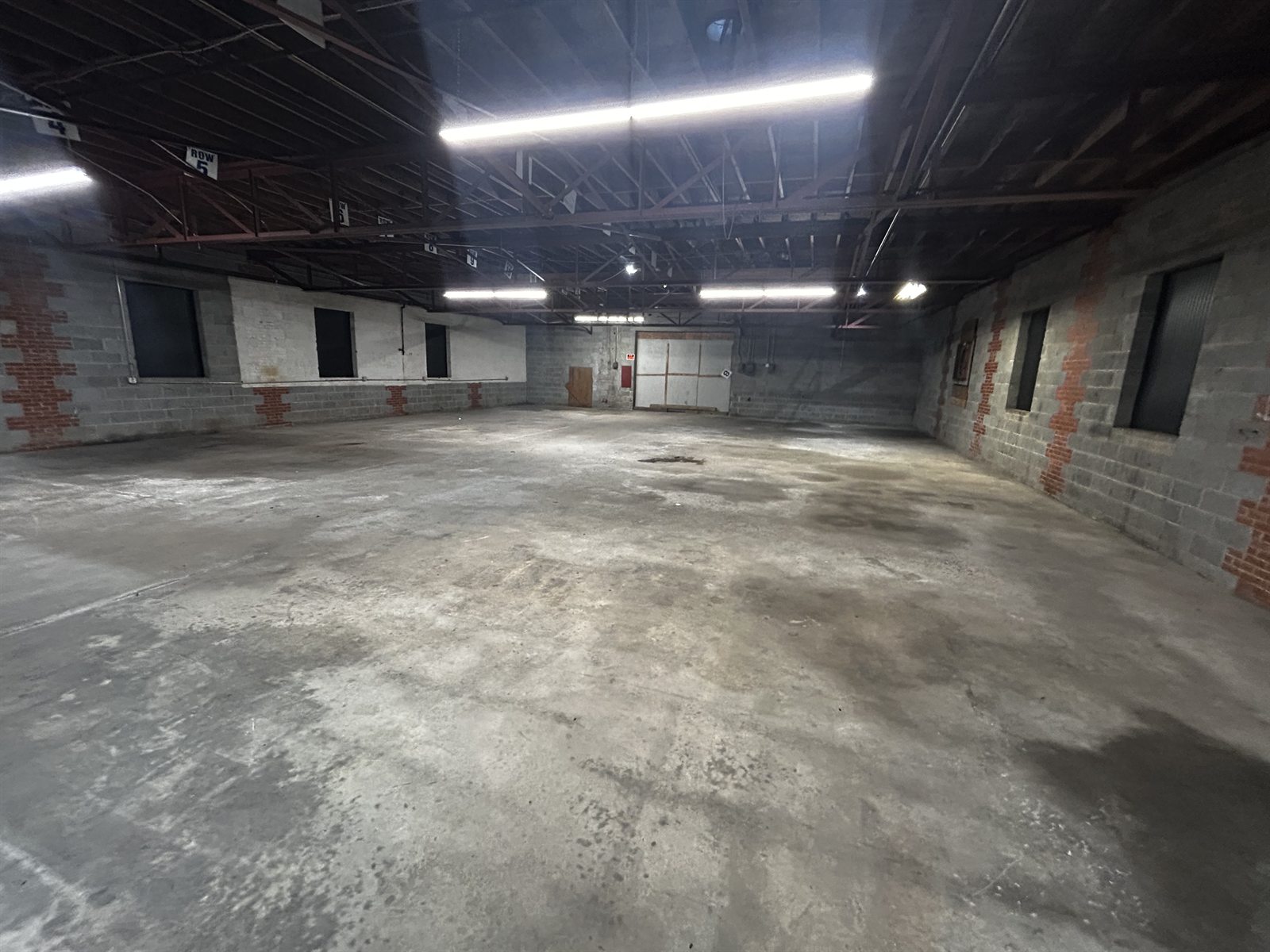 Second interior view of an available suite at 314 Mandustry Street showing a clear concrete floor, block walls, an overhead door at the far end, and exposed roof trusses