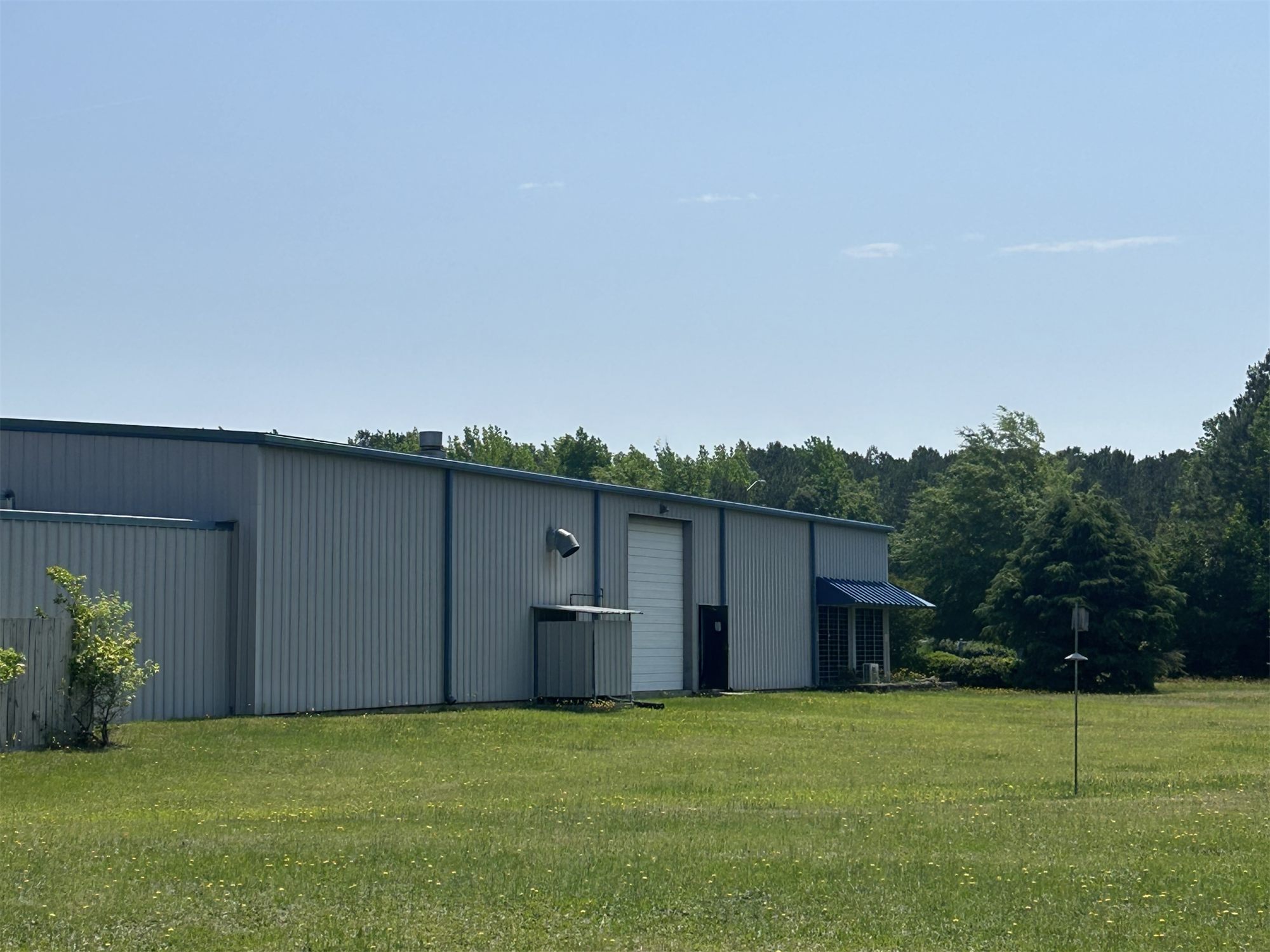 Side elevation of 4475 Technology Drive NW, a gray metal industrial building with a white roll-up drive-in door, a blue awning over the office entry, and a mowed lawn in front