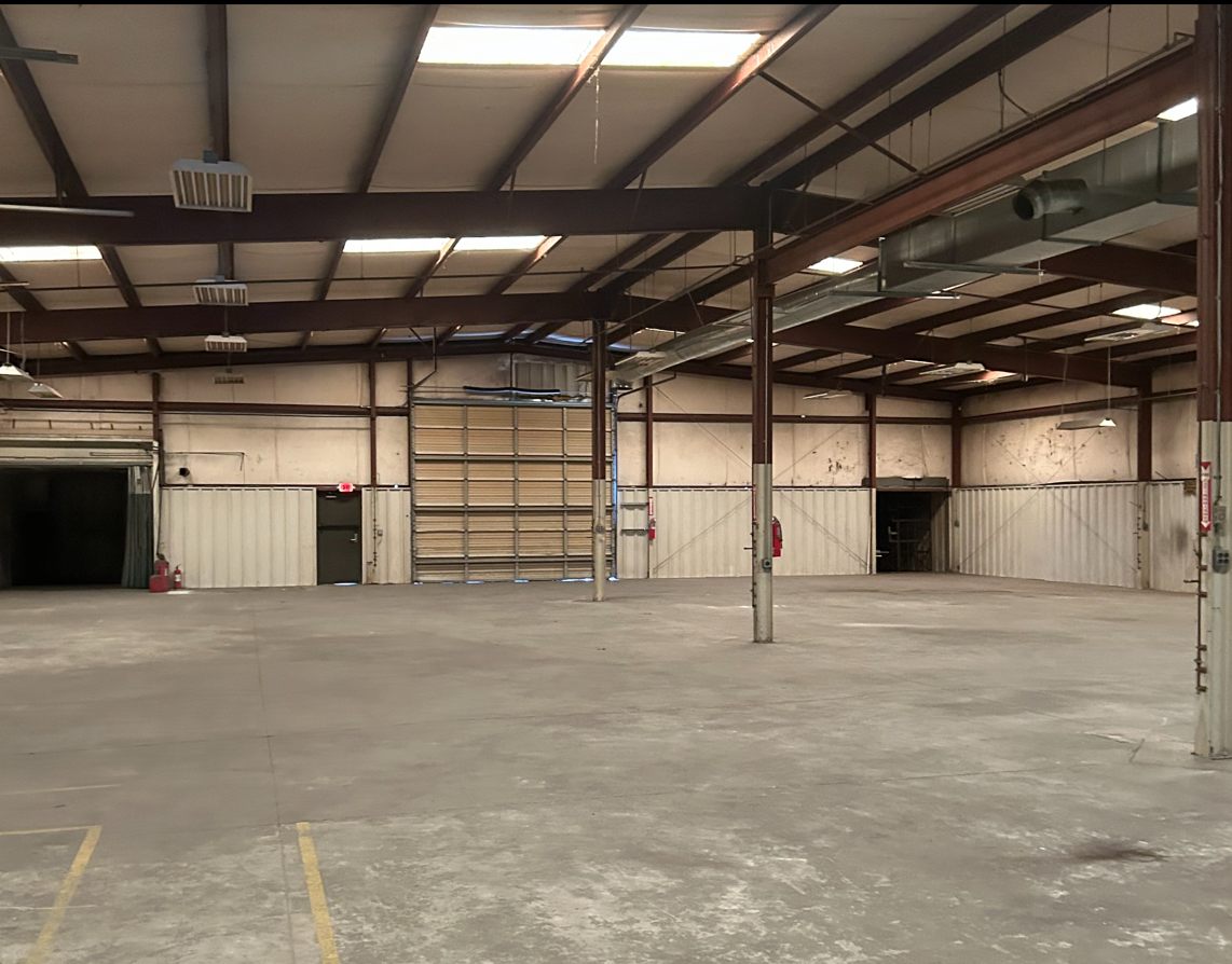 Warehouse interior at 4475 Technology Drive NW with an open concrete floor, red steel columns and roof framing, skylights, overhead heaters, and a sectional drive-in door on the far wall