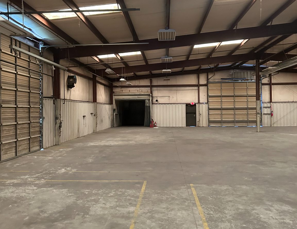 Warehouse at 4475 Technology Drive NW with drive-in doors on two walls, an opening through to another bay, skylights, and striped lines on the concrete floor