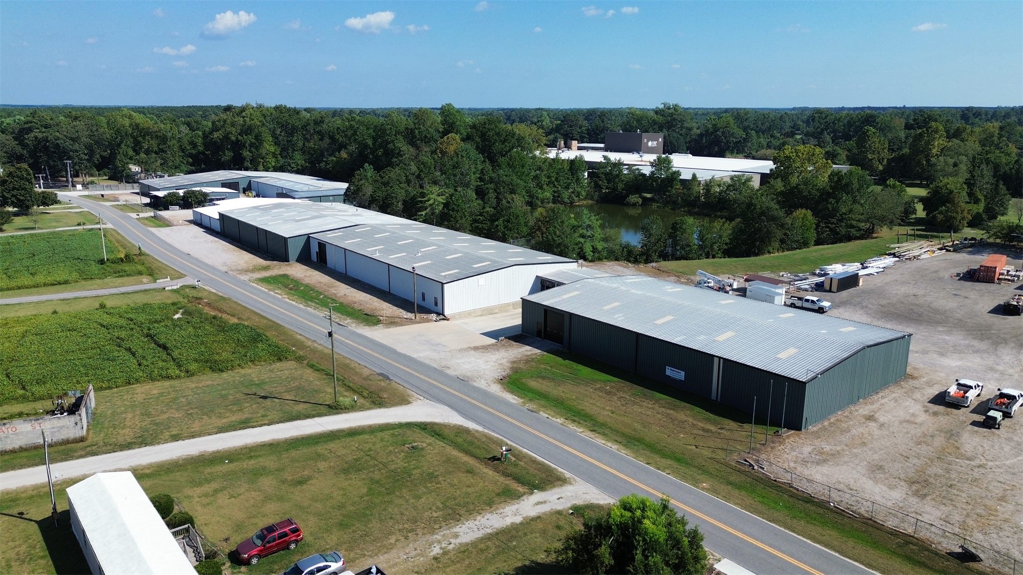 Aerial view of the 4734 Potato House Court industrial park in Wilson, North Carolina: a line of metal warehouse buildings along the road, with the gravel storage yard in front and a pond and woods behind