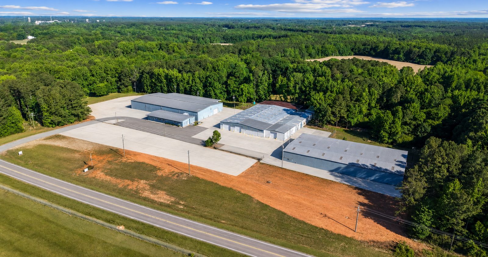 Aerial view over the 6863 NC-56 campus in Franklinton, showing the four buildings, concrete truck courts, and graded laydown yard along the highway
