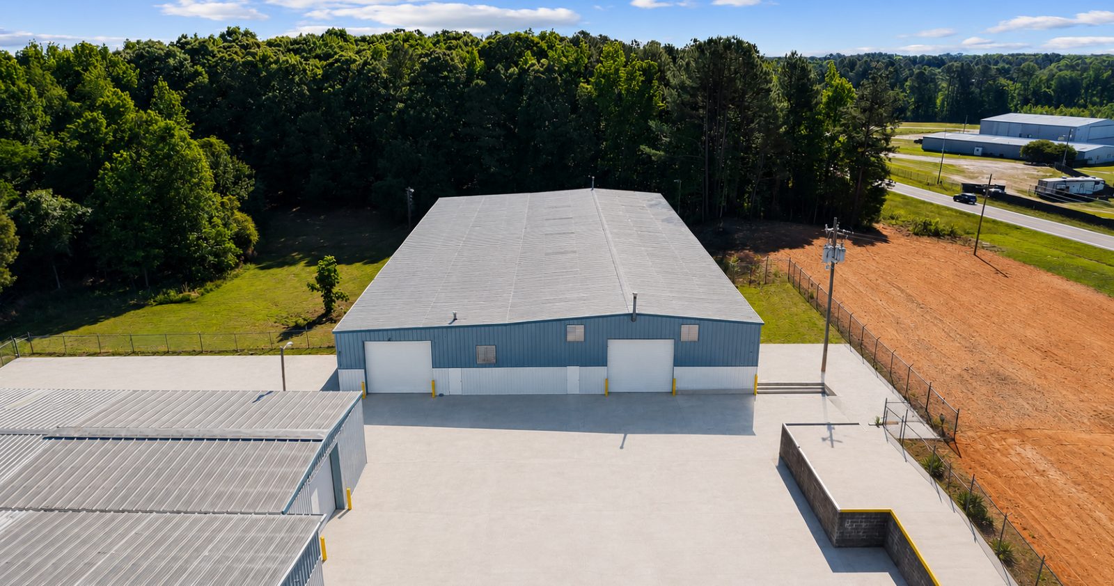 Aerial view of drive-in overhead doors along a warehouse at 6863 NC-56, fronting the concrete yard with the graded laydown area beyond