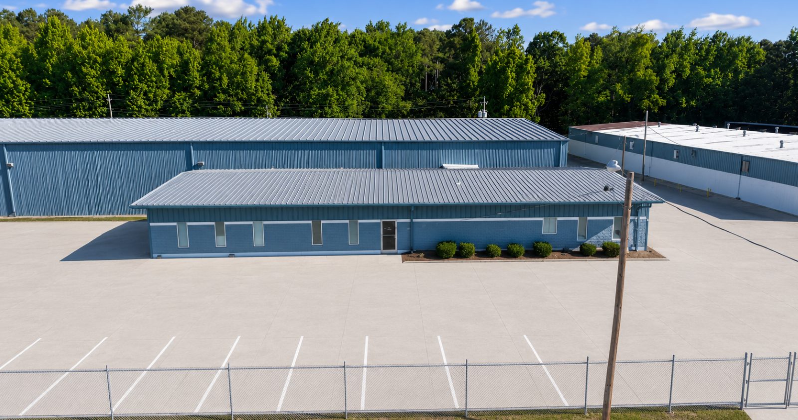 Ground-level view of the blue metal office and warehouse buildings at 6863 NC-56 across a striped concrete parking area