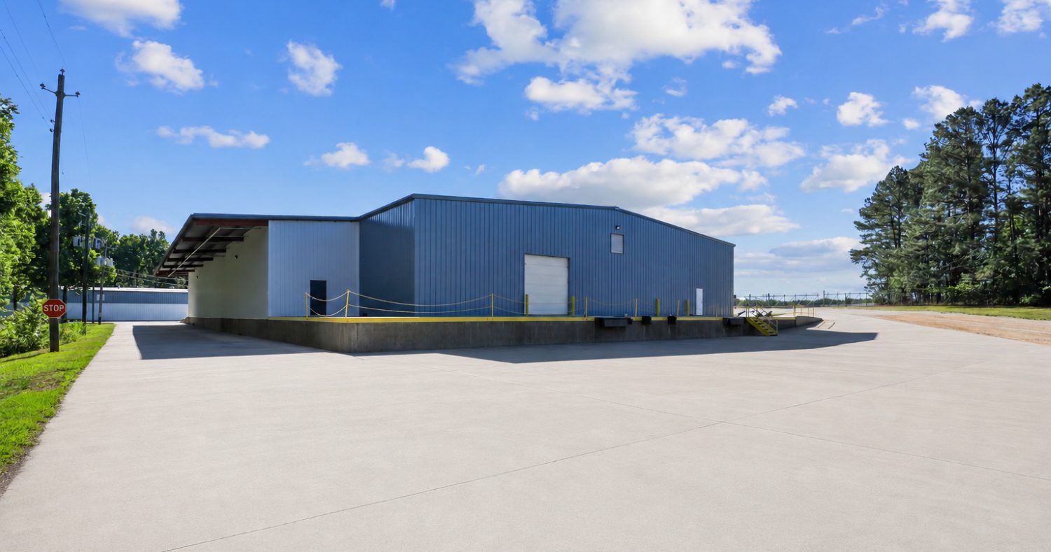 Covered concrete loading dock along a blue metal warehouse at 6863 NC-56, opening onto a wide concrete apron