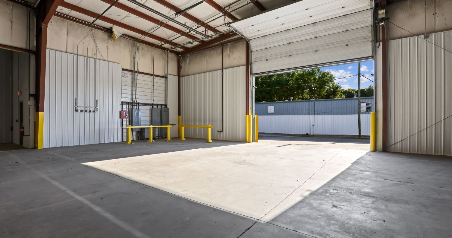 Long warehouse bay at 6863 NC-56 lined with roll-up doors along the wall, under exposed steel framing and high-bay lighting