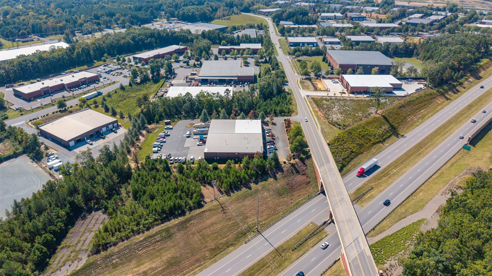 Aerial of 7204 Stinson Hartis Road and the surrounding industrial park, with the Monroe Expressway passing under the Stinson Hartis Road overpass and more industrial and flex buildings beyond