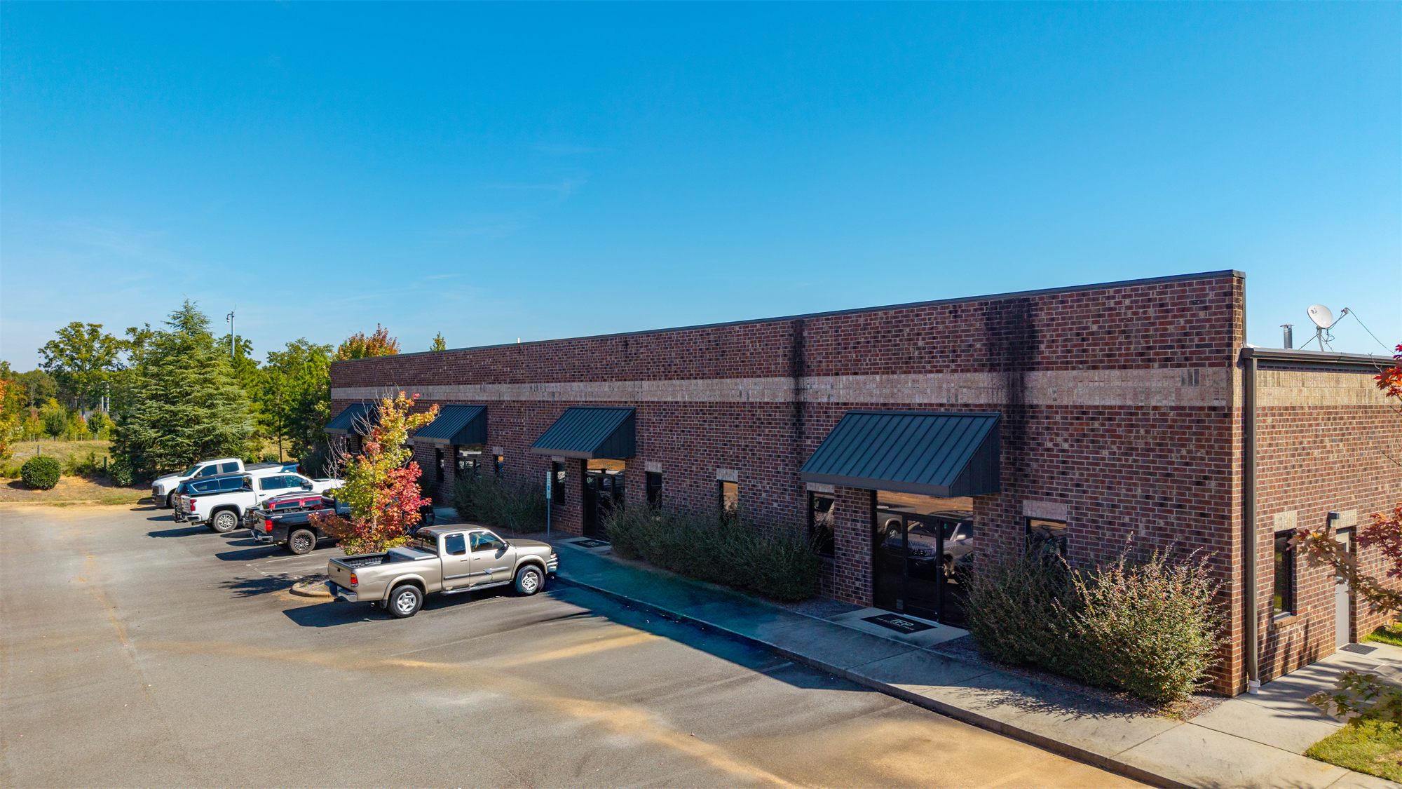 Brick front of 7204 Stinson Hartis Road with storefront entries under dark metal awnings, landscaping, and parking along the building