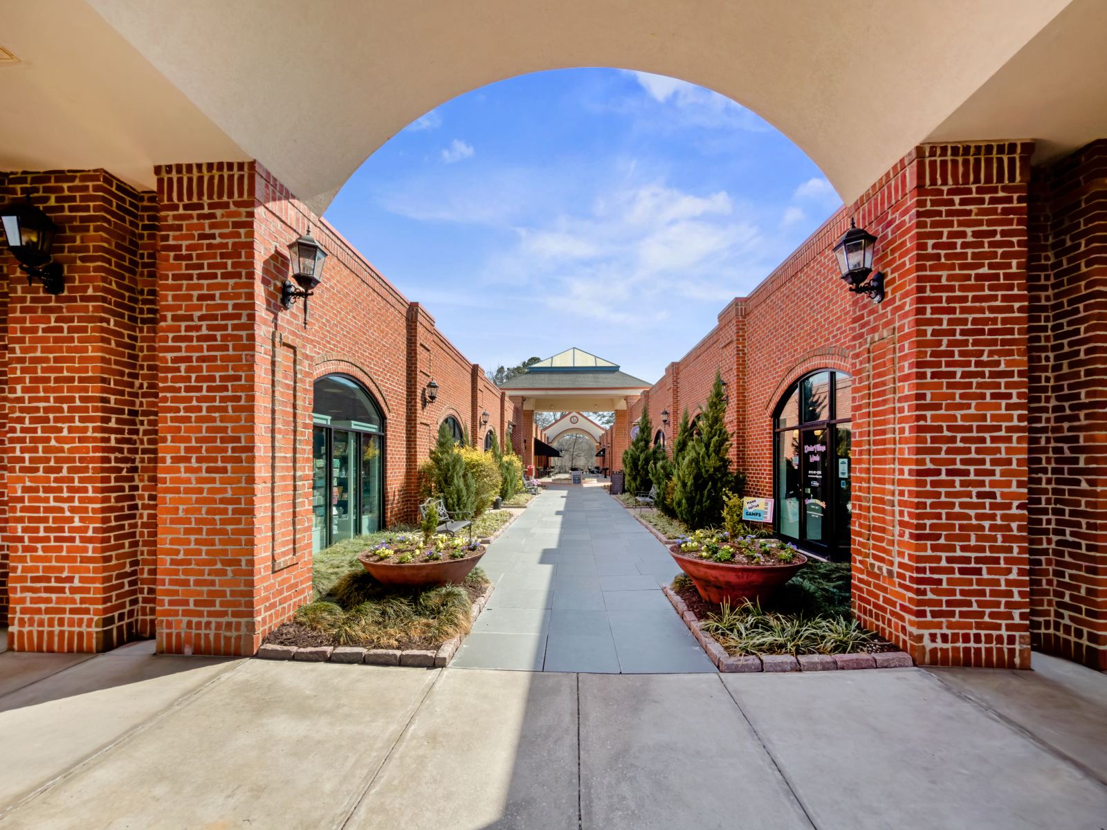 View through the brick archway at Lochmere Pavilion into the landscaped interior courtyard walk lined with storefronts