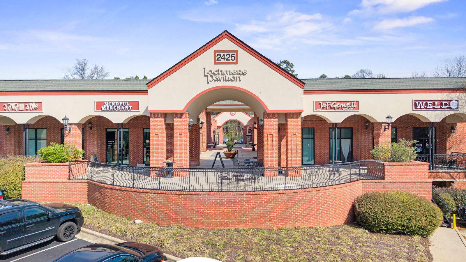 Front elevation of Lochmere Pavilion, with the 2425 Lochmere Pavilion gable sign over the arched courtyard entry and storefronts on either side
