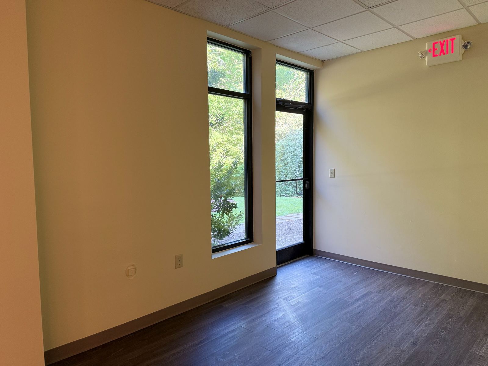 Private room in Suite 104 with a full-height window and a glass exterior door opening to the landscaped grounds