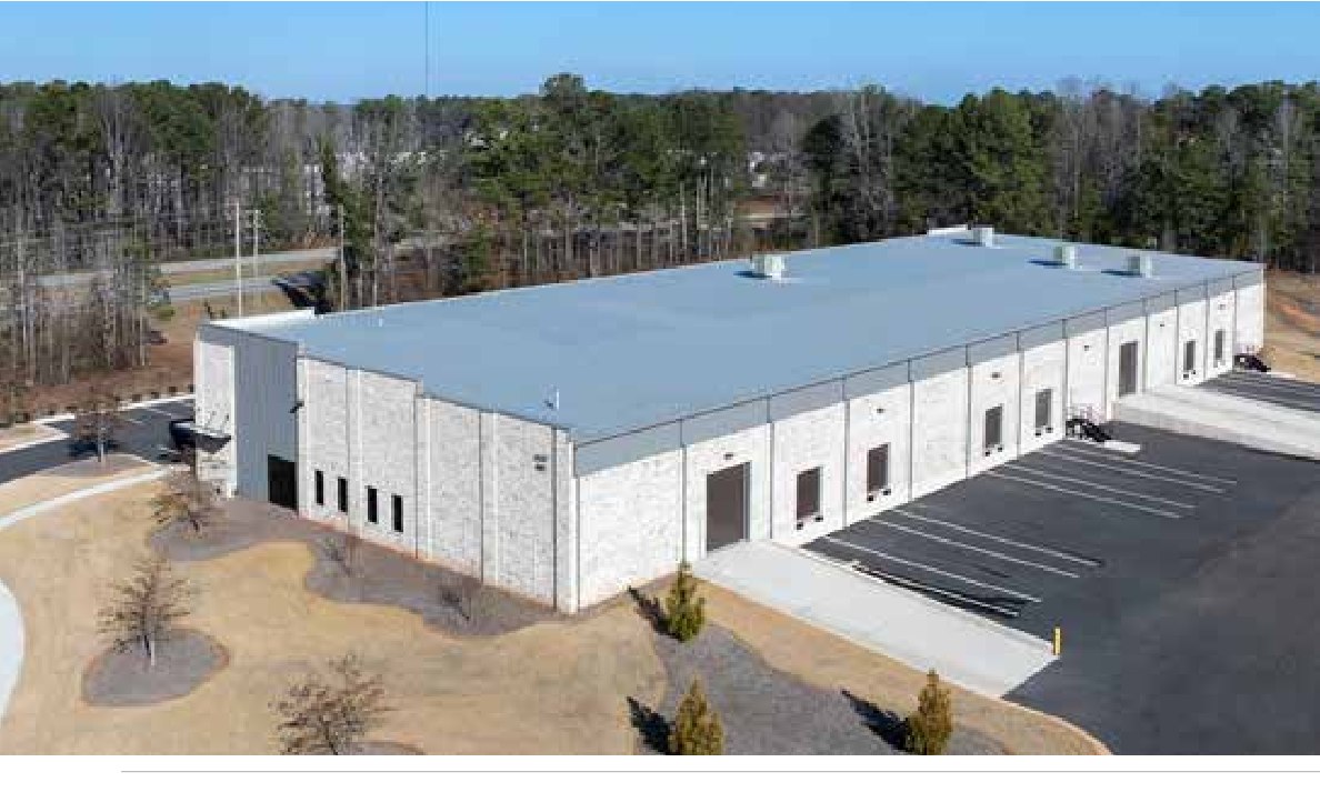 Aerial view of 74 South Business Park, the completed Woodlands prototype, showing its shallow rectangular footprint, roof, surrounding parking, and drive aisles