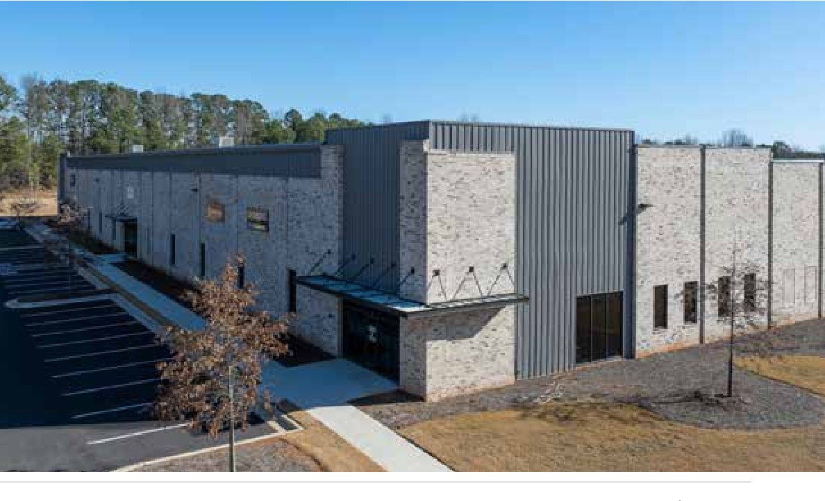 Angled view of 74 South Business Park, the completed Woodlands prototype, showing the canopied storefront entries, brick and metal facade, and paved drive aisle